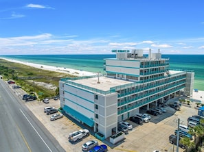 Un immeuble à plusieurs étages doté d’un parking, situé près d’une plage aux eaux d’un bleu cristallin.