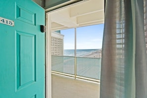 Une porte turquoise avec une plaque portant un numéro, un balcon doté d’une rambarde en métal et une vue sur la mer.