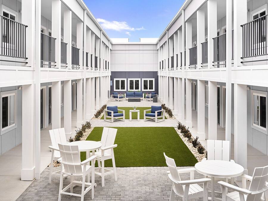 Un patio moderno con mobiliario blanco, un área de estar central y un pequeño césped.