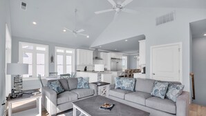 Een moderne woonkamer met een grijze bank, een salontafel en een eethoek, met een keuken op de achtergrond.