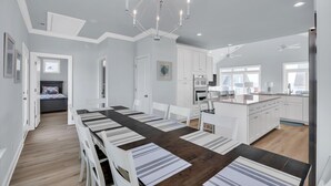 Een moderne keuken met witte kastjes, een houten eettafel met geribbelde placemats en een kroonluchter.