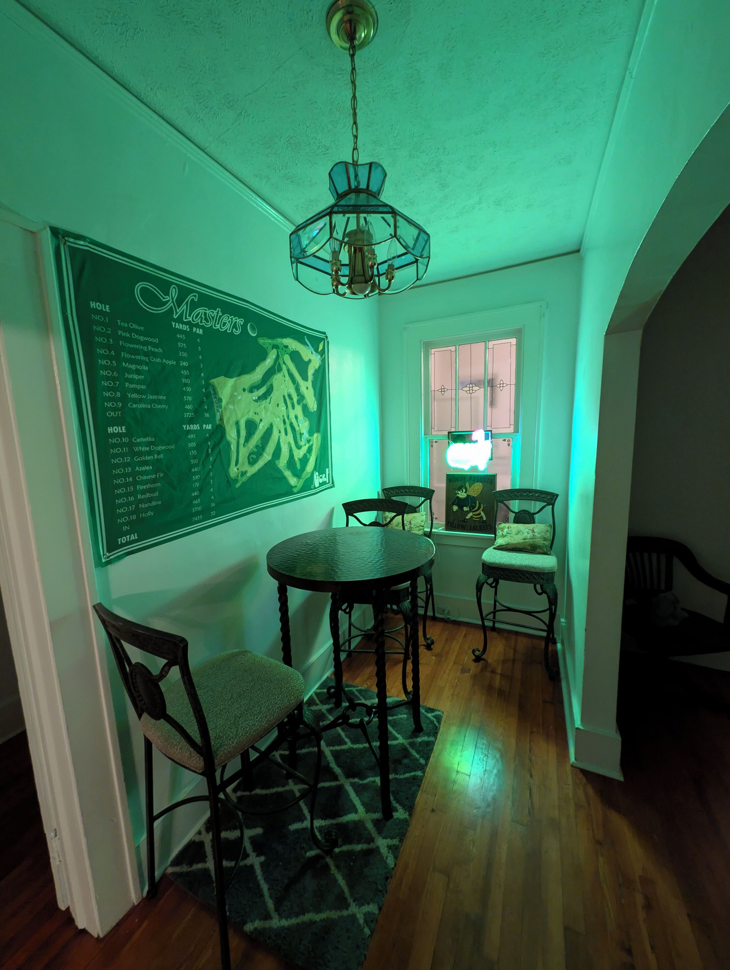Un coin repas avec une table ronde, deux chaises, un lustre et un mur sur lequel est affiché un menu sur un tableau noir vert.