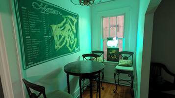 Un coin repas avec une table ronde, deux chaises, un lustre et un mur sur lequel est affiché un menu sur un tableau noir vert.