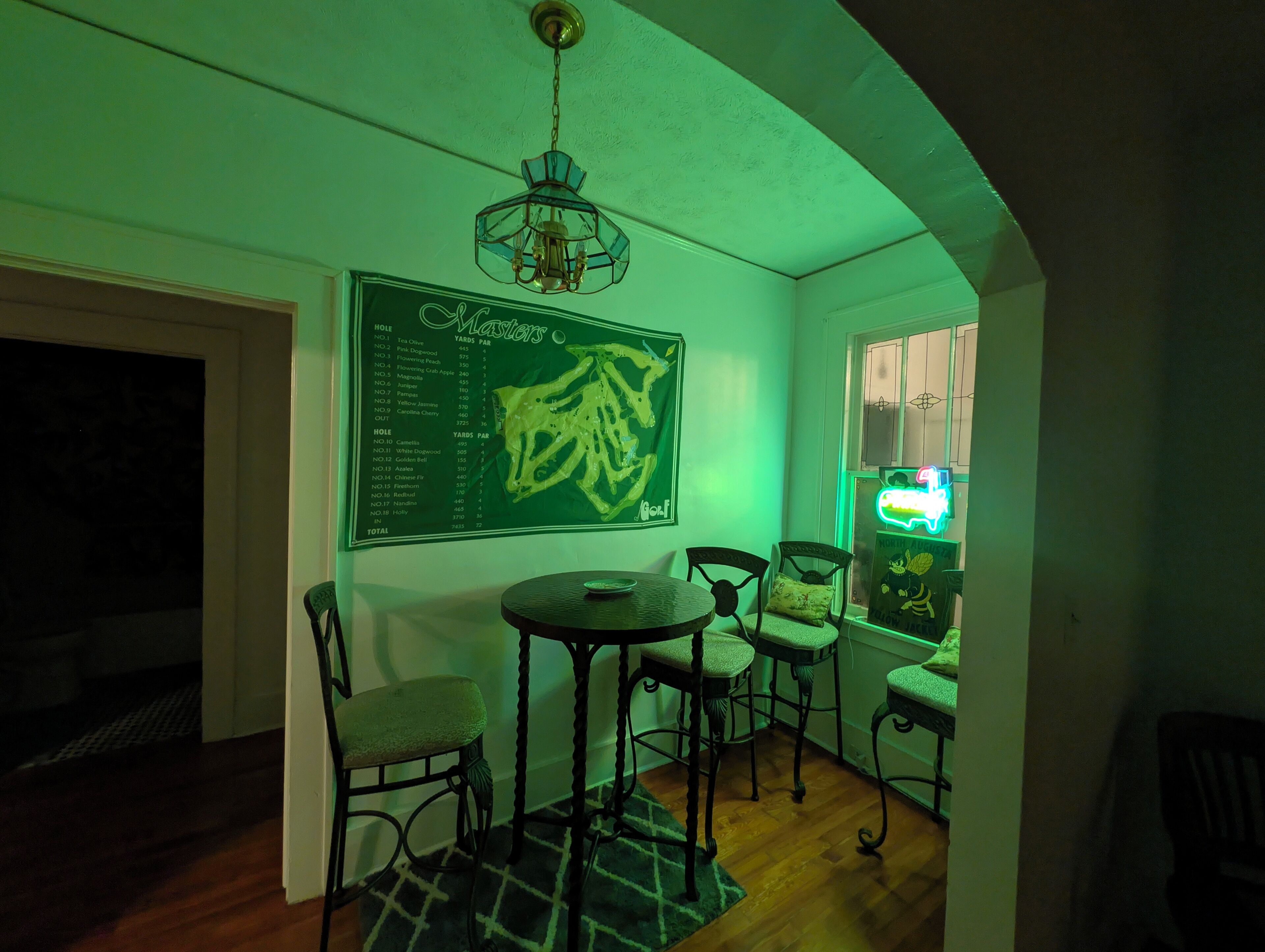 A room with a green wall, a chalkboard with a list, a chandelier, and a neon sign.