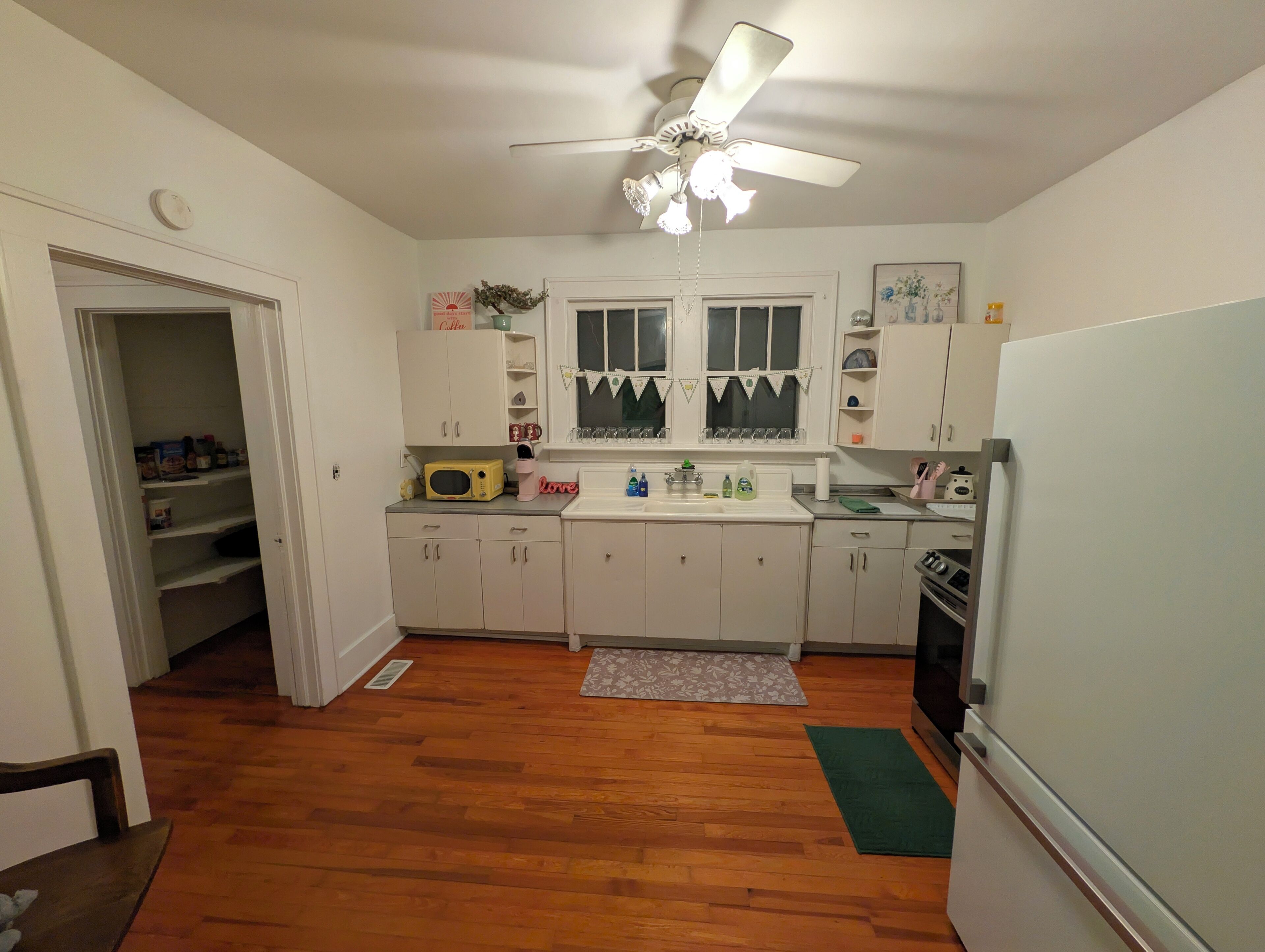 Une cuisine avec des meubles blancs, un four à micro-ondes, un réfrigérateur et un ventilateur de plafond.