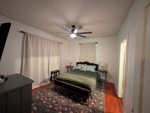 A bedroom with a bed, two bedside tables with lamps, a ceiling fan, and a patterned rug. - Casey's Cottage- Georgia Ave (North Augusta)
