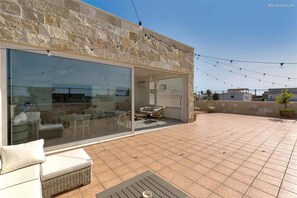 A modern outdoor patio with a stone wall, a glass sliding door leading to an interior space, and a seating area with a table and chairs. - 2106 B B Le Radici Del Salento - Camera Matrimoniale (San Pancrazio Salentino)