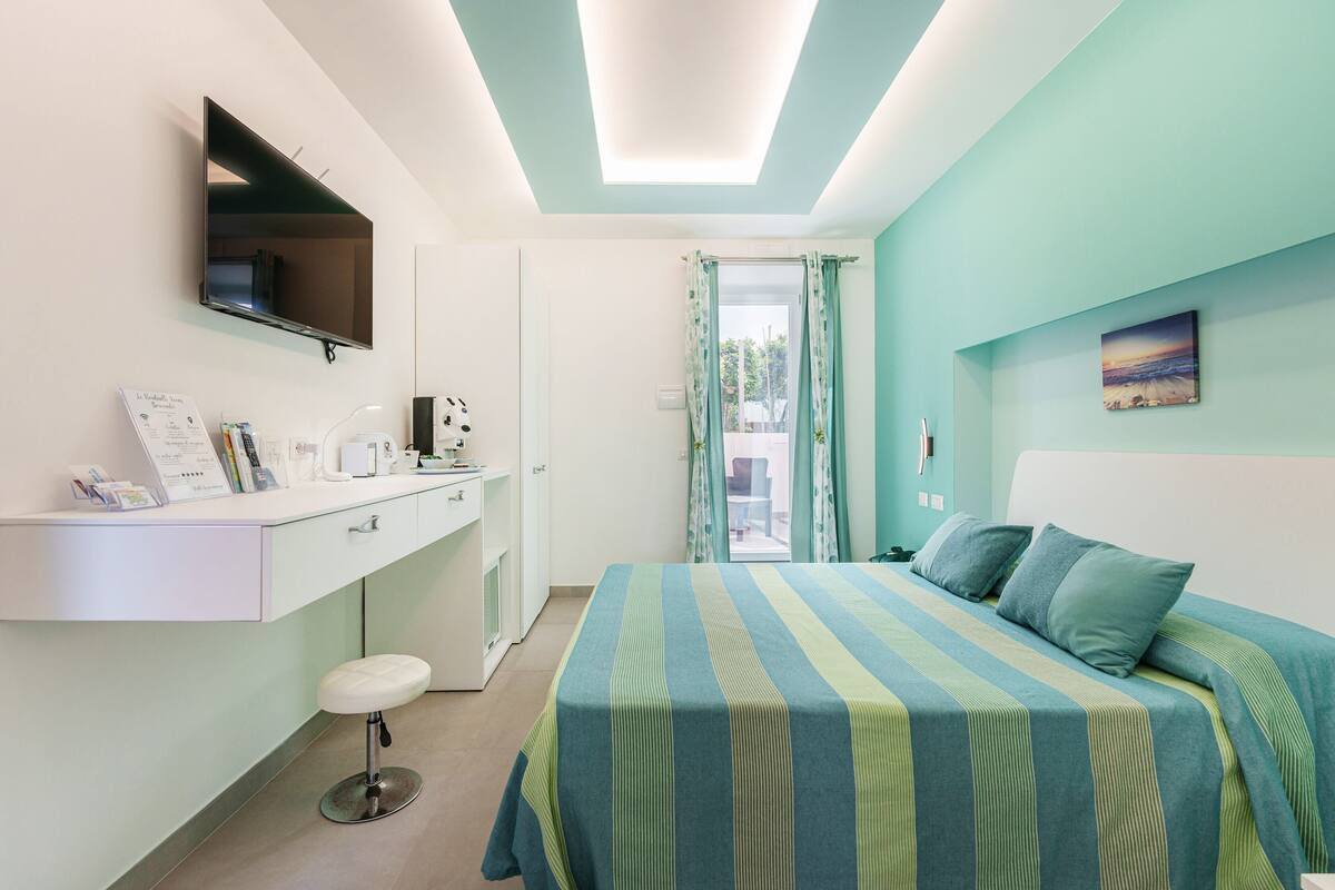 A bedroom with a bed, a desk, a chair, and a window with curtains.