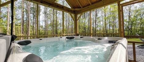 A hot tub with a wooden deck and a forest view.