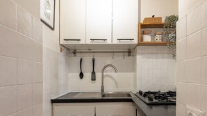 Ett kompakt kök med vita skåp, en svart bänkskiva, en diskho i rostfritt stål och en gasspis.