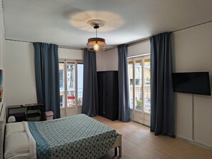 A hotel room with a bed, a desk, a chair, a TV on the wall, and a balcony with curtains. - B&B Napoli Fuorigrotta (Naples)