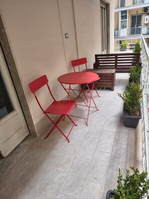 A balcony with a red metal table and chairs, a wooden bench, and potted plants. - B&B Napoli Fuorigrotta (Naples)