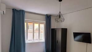 Et værelse med en seng, et skab, et fjernsyn og et vindue med gardiner.