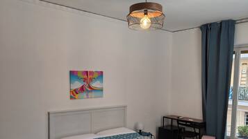 Un dormitorio con cama, escritorio, silla, lámpara, ventilador de techo y ventana con cortinas.