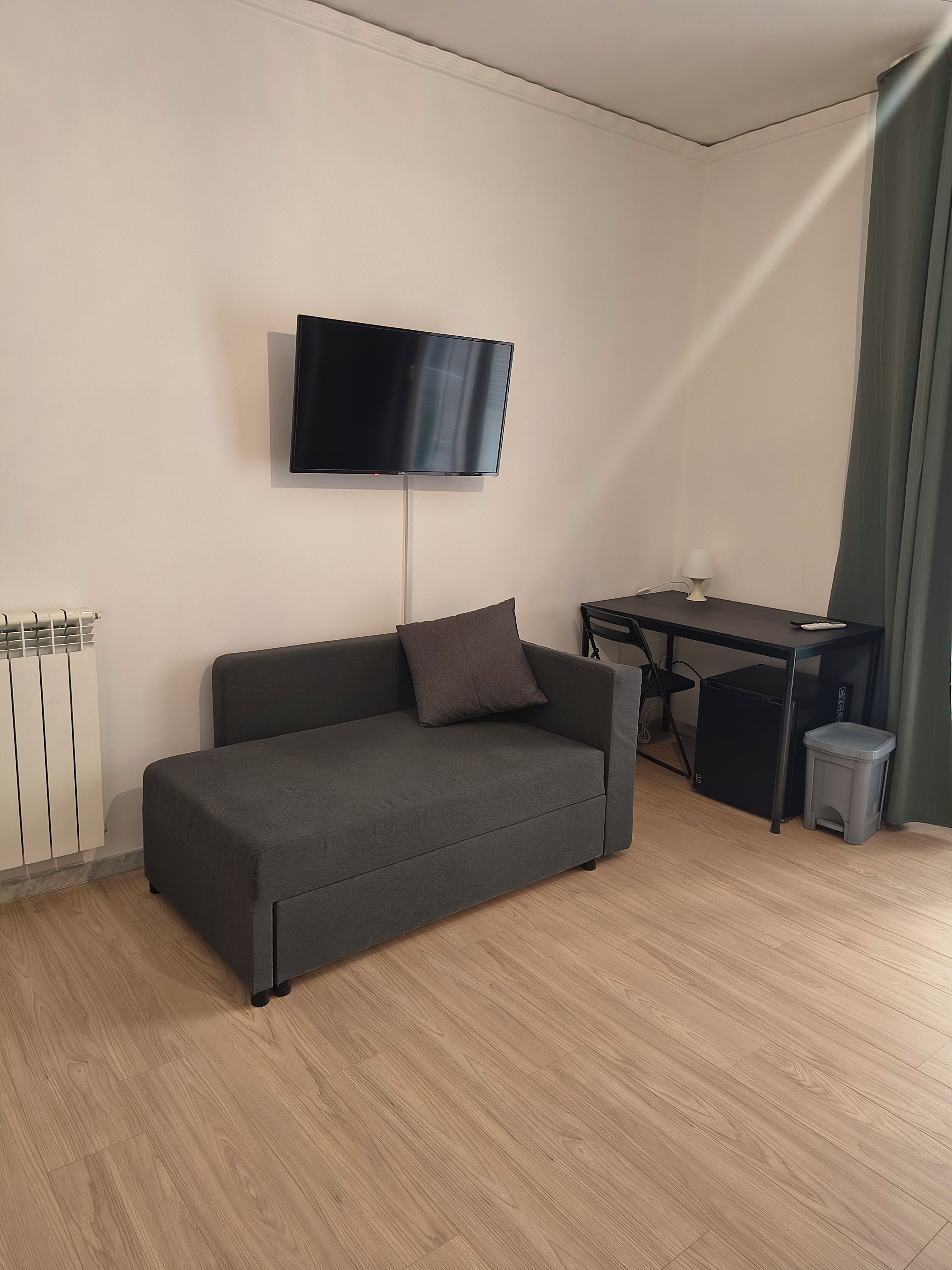 Una sala de estar moderna con un sofá, un televisor de pantalla plana montado en la pared, un escritorio y un cesto de basura.