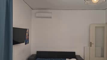 Une pièce comprenant un lit, un téléviseur fixé au mur, un luminaire au plafond et une porte.