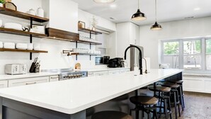 Une cuisine moderne dotée d’un grand îlot central, de tabourets de bar, de luminaires suspendus et d’un sol en briques.