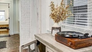 Une pièce rustique aux murs en briques apparentes, avec un meuble en bois doté de tiroirs, un radiateur et une fenêtre équipée de stores.