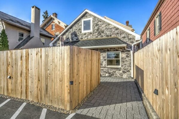 A stone house with a wooden fence, a paved driveway, and a clear blue sky.