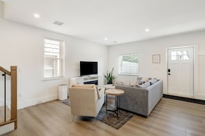 A modern living room with a grey sofa, a small round table, a TV on a white stand, and a staircase on the left. - The Loft at Legacy Manor/Minutes from Sight&Sound and Downtown Lancaster (Lancaster)