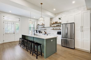 A modern kitchen with a central island, bar stools, a stainless steel refrigerator, and white cabinetry.