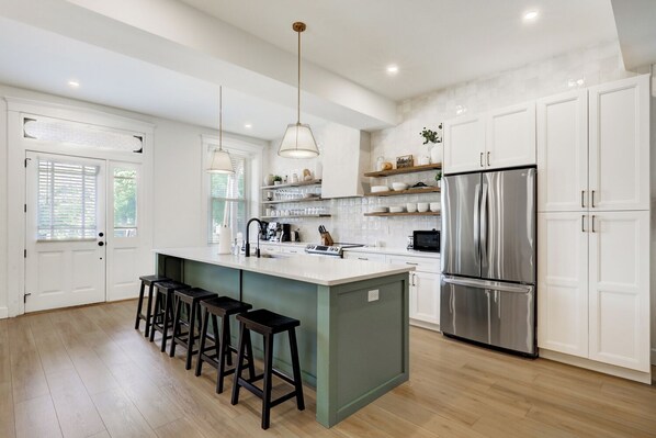 A modern kitchen with a central island, bar stools, a stainless steel refrigerator, and white cabinetry.