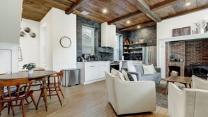 Una cocina moderna con armarios blancos, un comedor con mesa y sillas de madera, y una sala de estar con sofá blanco y chimenea.