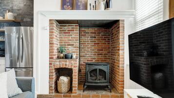 A living room with a brick fireplace, a television, and a modern kitchen with a stainless steel refrigerator.
