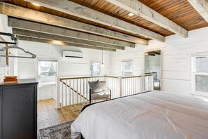 A bedroom with a large bed, wooden beams, a chair, and a view of the outdoors. - The Cottage at Legacy Manor (Lancaster)