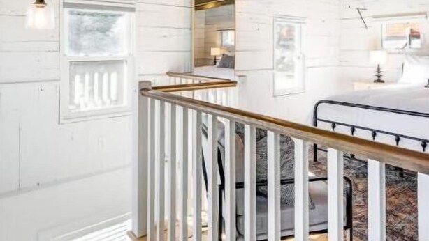 A high-ceilinged room with exposed wooden beams, a white-painted interior, and a staircase with a wooden railing. - The Cottage at Legacy Manor (Lancaster)