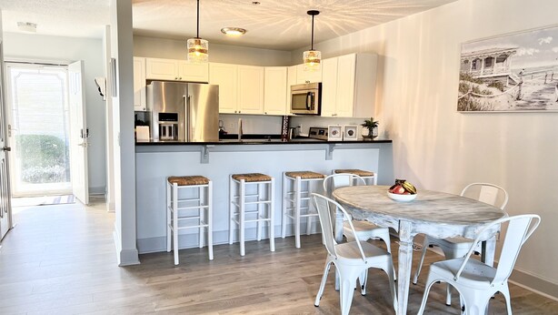 Une cuisine moderne avec des meubles blancs, des appareils en acier inoxydable et un coin repas comprenant des chaises blanches et une table en marbre.