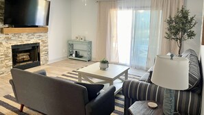 Un salon équipé d’un téléviseur à écran plat, d’une cheminée, d’un canapé, d’une table basse et d’un divan à rayures.