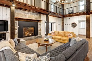 A spacious living room with a stone fireplace, leather sofas, and a high ceiling with exposed beams. - Legacy Manor-Sleeps 26-9 minutes to Sight&Sound,16 Minutes to Downtown Lancaster (Lancaster)