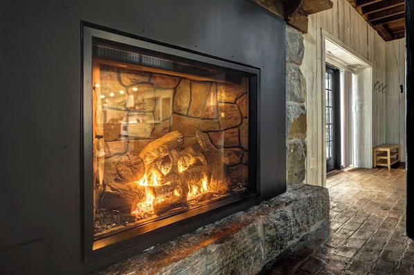 Una chimenea de piedra con frente de vidrio, un banco de madera y un interior rústico.
