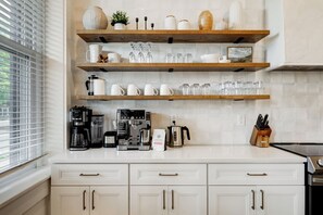 A kitchen with white cabinets, wooden shelves, a coffee maker, and a kettle.