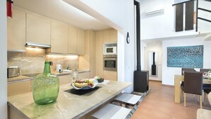 A modern kitchen with a marble countertop, a large green bottle, and a fruit bowl. There is a dining area with a table and chairs, and a black stove in the background. - Ca Na Lida - Two Bedroom Villa, Sleeps 4 (Mallorca)