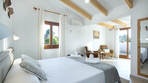Een slaapkamer met een groot bed, een stoel, een tafel en een raam met gordijnen.