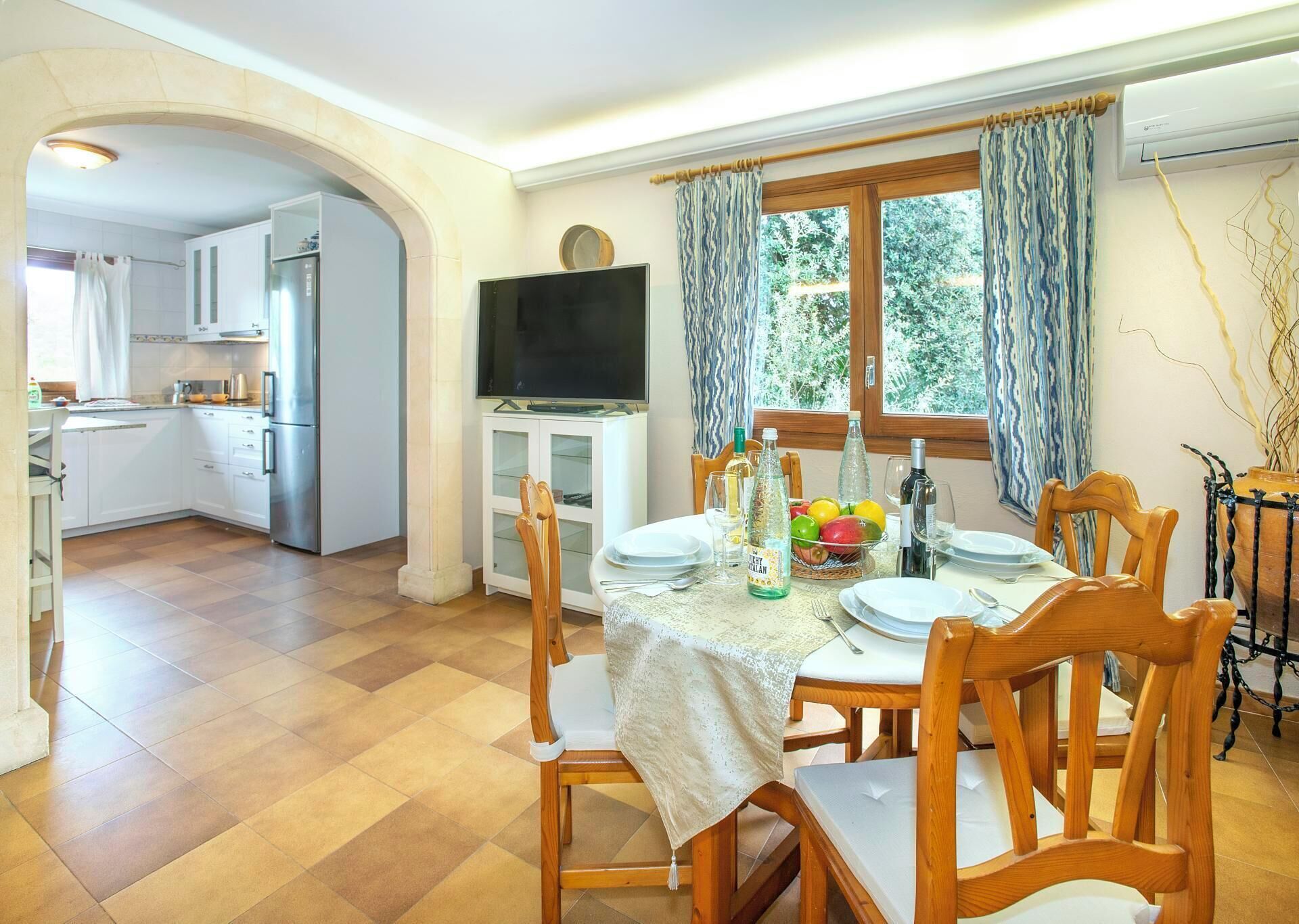 A dining area with a table set for four, a television, and a kitchen in the background.