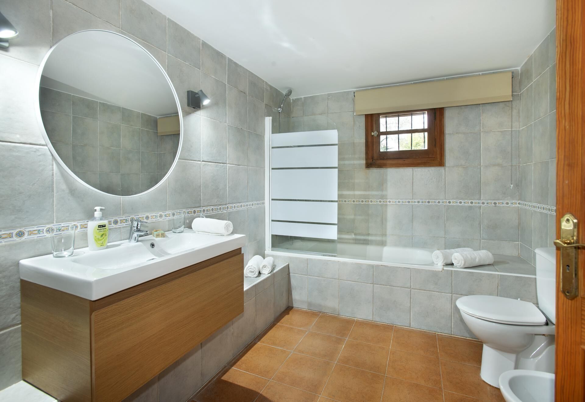 Une salle de bain moderne avec un grand miroir, un lavabo avec un meuble-vasque en bois, une baignoire et des toilettes.