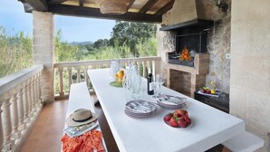Un espace extérieur aménagé pour les repas, avec une table pour quatre personnes, un barbecue et une vue sur la campagne.
