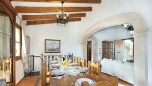 Un coin repas avec une table en bois dressée pour quatre personnes, entourée de chaises en bois. Un arc en plein cintre donne accès à une autre pièce.