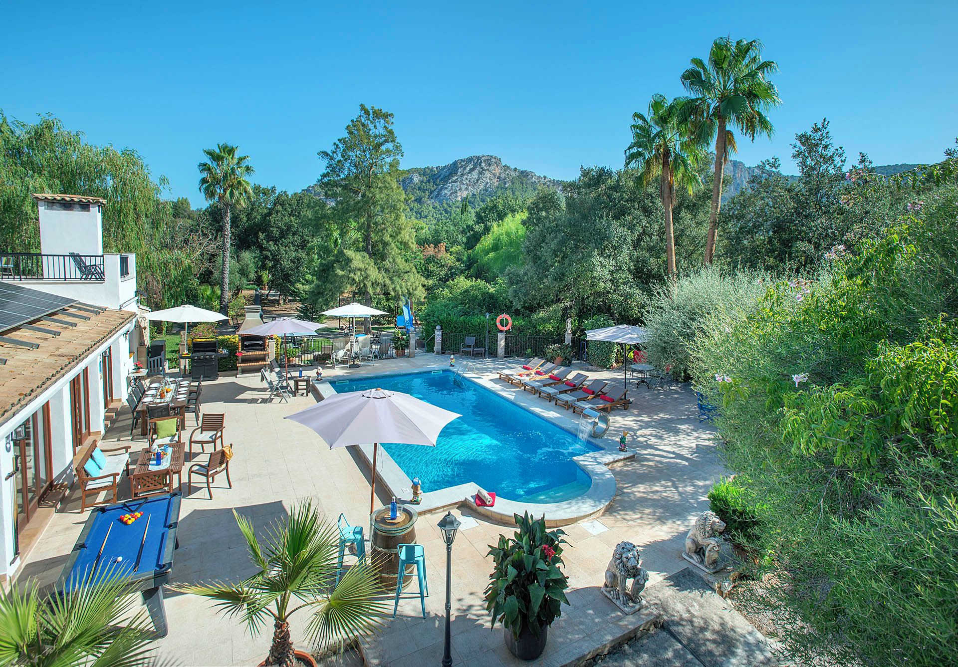 A pool area with lounge chairs, a pool table, and a mountain backdrop.