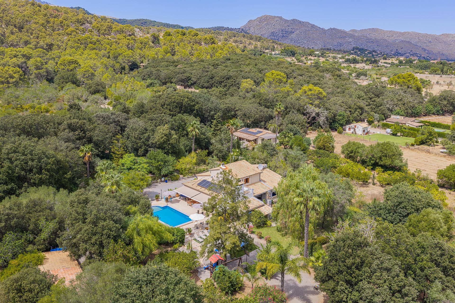 A residential area with a swimming pool, surrounded by dense greenery and hills in the background.