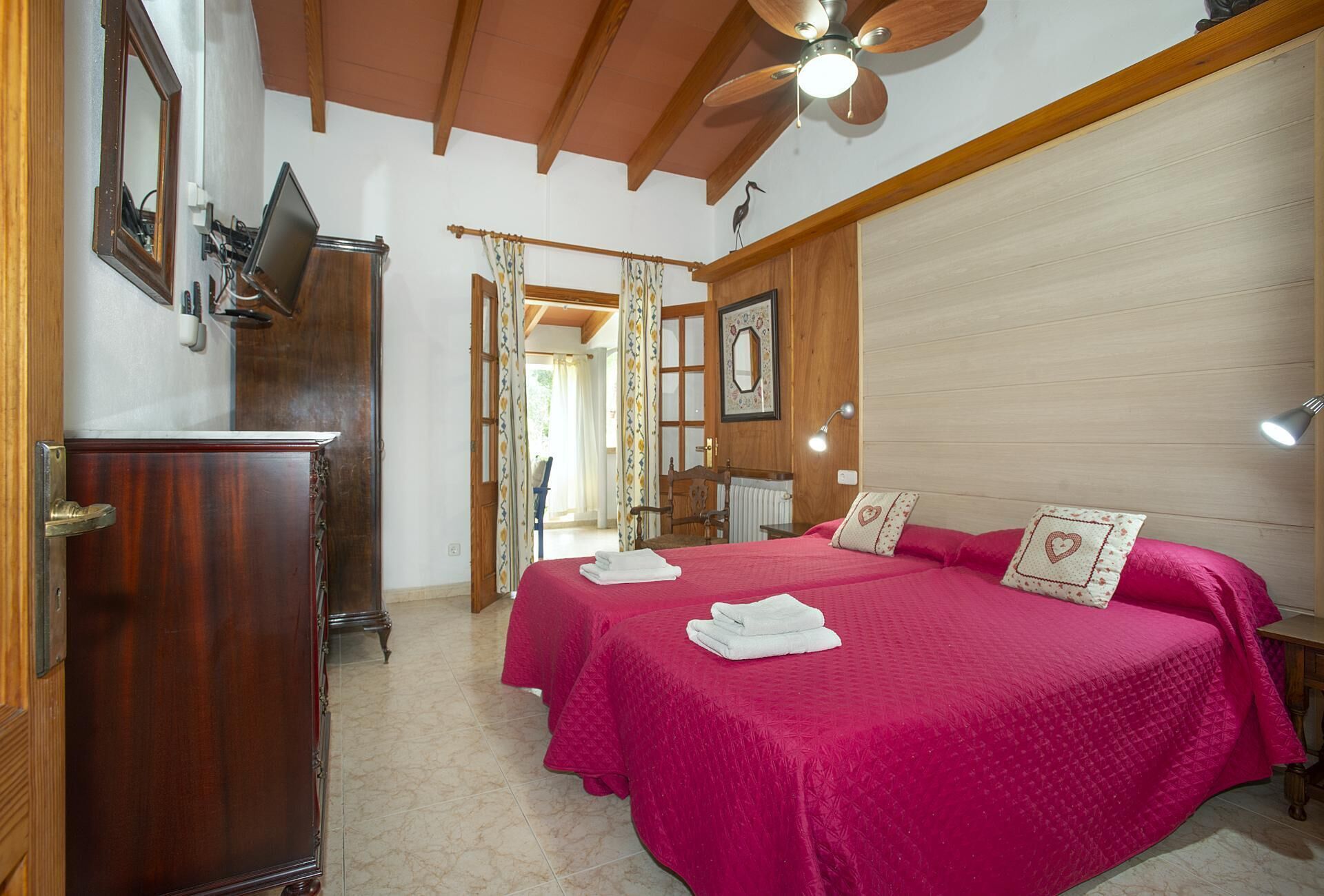 A bedroom with two beds, a wooden wardrobe, a ceiling fan, and a bathroom visible through an open door.
