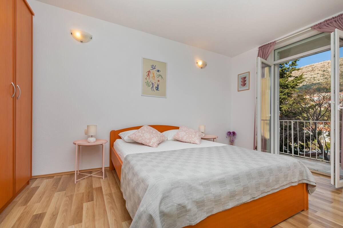 Un dormitorio con cama, mesitas de noche, una ventana con vistas y una puerta.