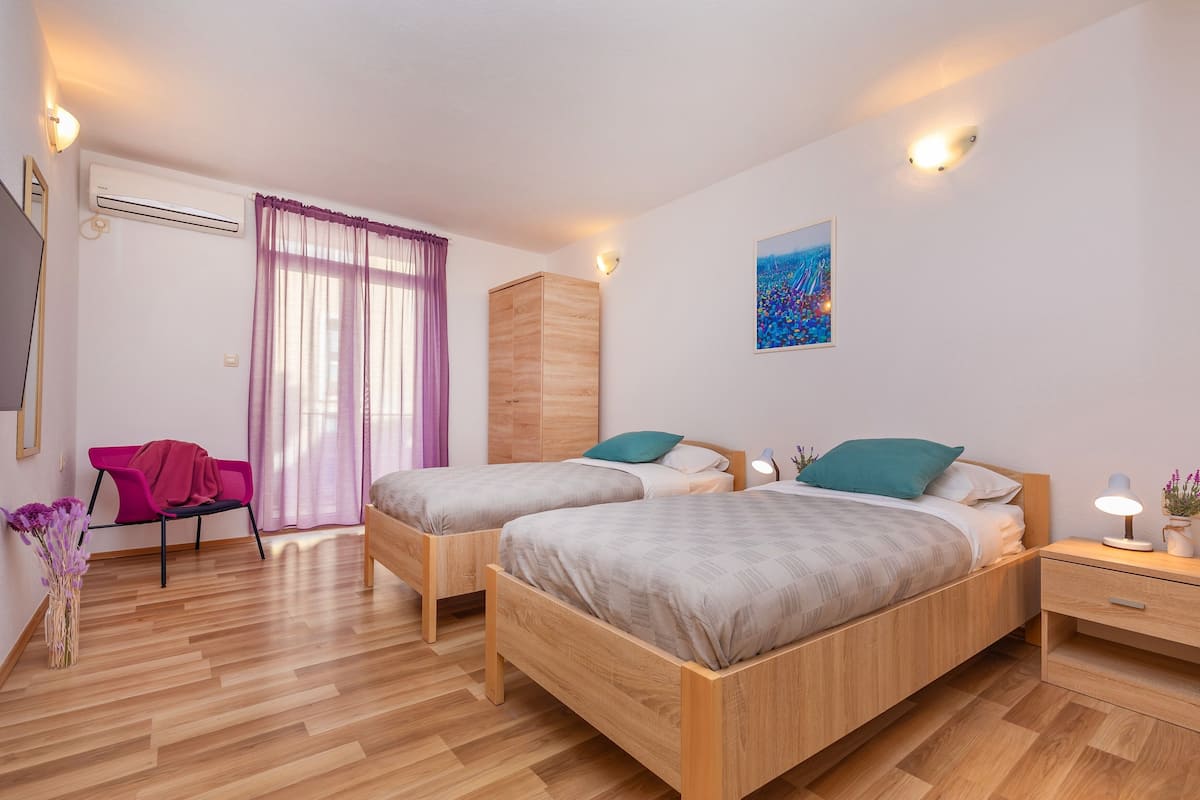 Un dormitorio con dos camas de madera, una mesita de noche con lámpara, un armario, una silla y un cuadro en la pared.