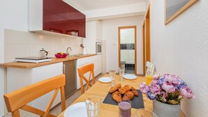 Una cocina moderna con armarios blancos, una encimera de madera y un comedor con una mesa dispuesta para dos personas. Hay pasteles en la mesa y un florero con flores.