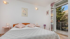 Un dormitorio con una cama, dos mesitas de noche, un ventanal con vistas a árboles y un cuadro en la pared.