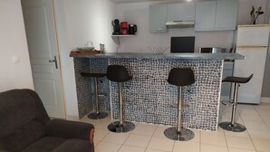 Une cuisine moderne avec un mur recouvert de carreaux, un bar intégré avec des tabourets et un coin salon avec un canapé.
