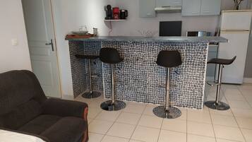 A modern kitchen with a tiled backsplash, a built-in bar area with stools, and a seating area with a sofa.